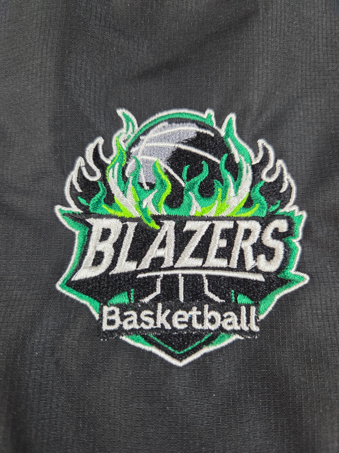 A close-up of a black athletic garment featuring a large embroidered 'BLAZERS Basketball' patch with green and white flames and a basketball graphic.